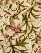 Embroidered floral fabric in pink and green on a cutter cream cotton background.