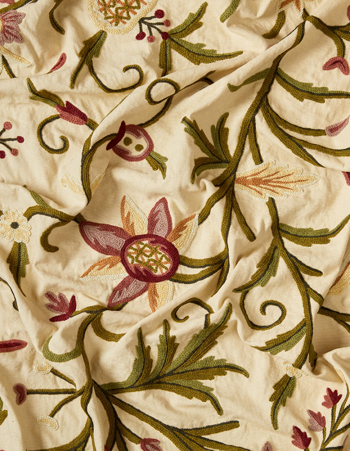 Embroidered floral fabric in pink and green on a cutter cream cotton background.