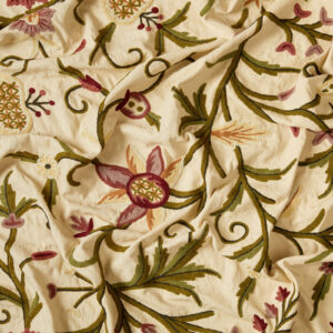 Embroidered floral fabric in pink and green on a cutter cream cotton background.
