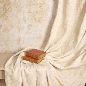 A swathe of cream on cream fabric draped in front of an antique stone wall with old books supporting the fabric.
